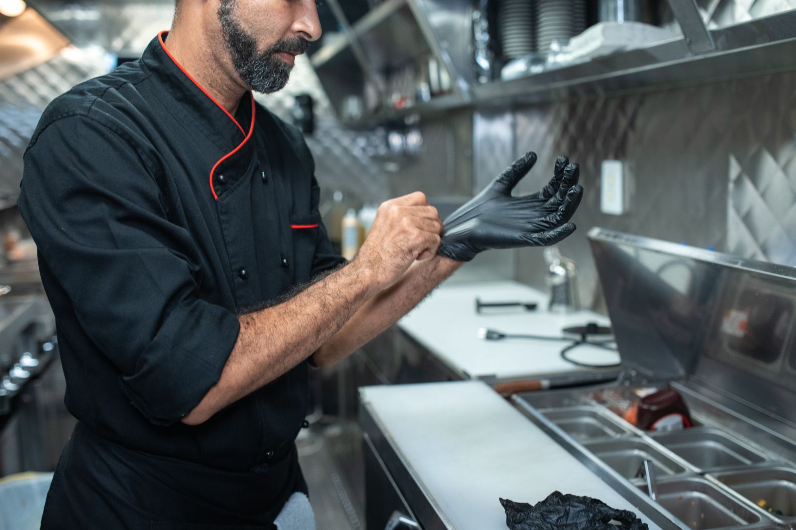 A chef pulling on disposable gloves before prep in a stainless-steel kitchen