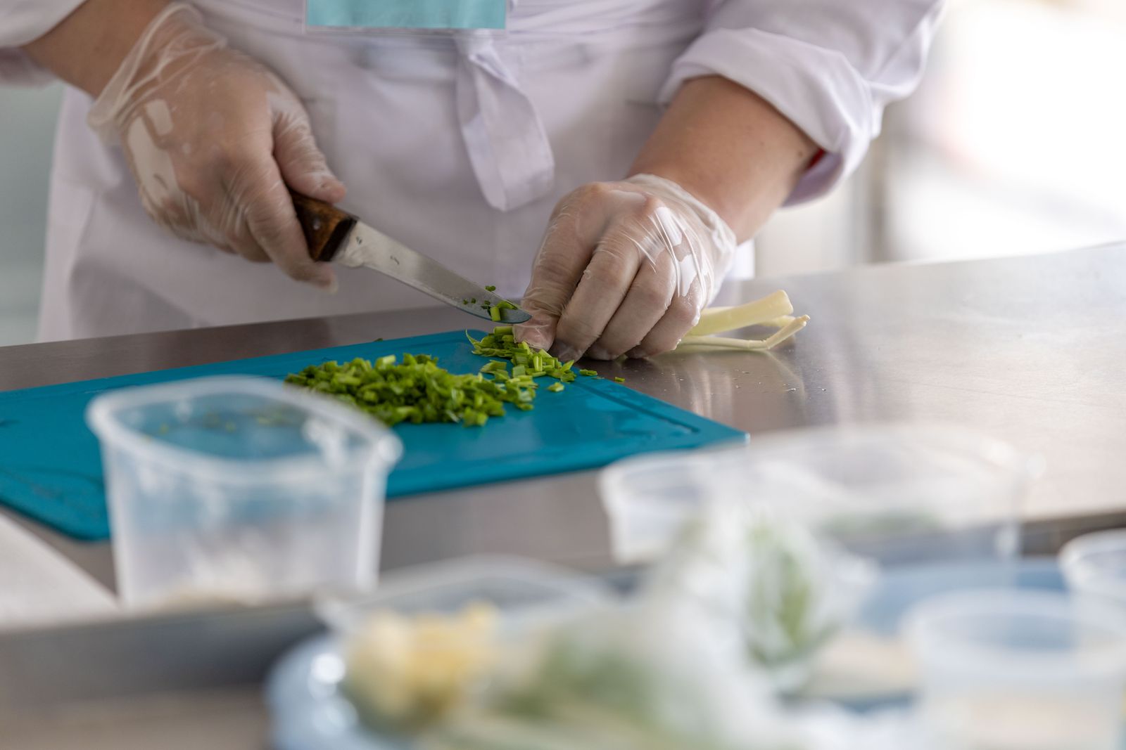 Gloved hands chopping herbs on a colour-coded board at a clean stainless-steel prep station